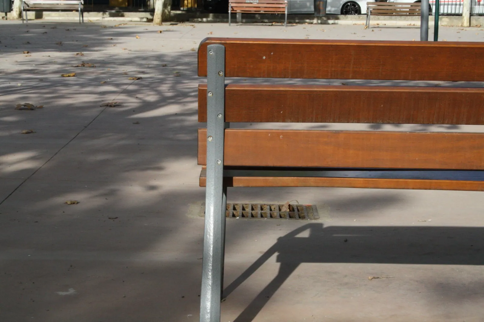 Banco de madera de un parque visto de cerca, con la plaza vacía al fondo
