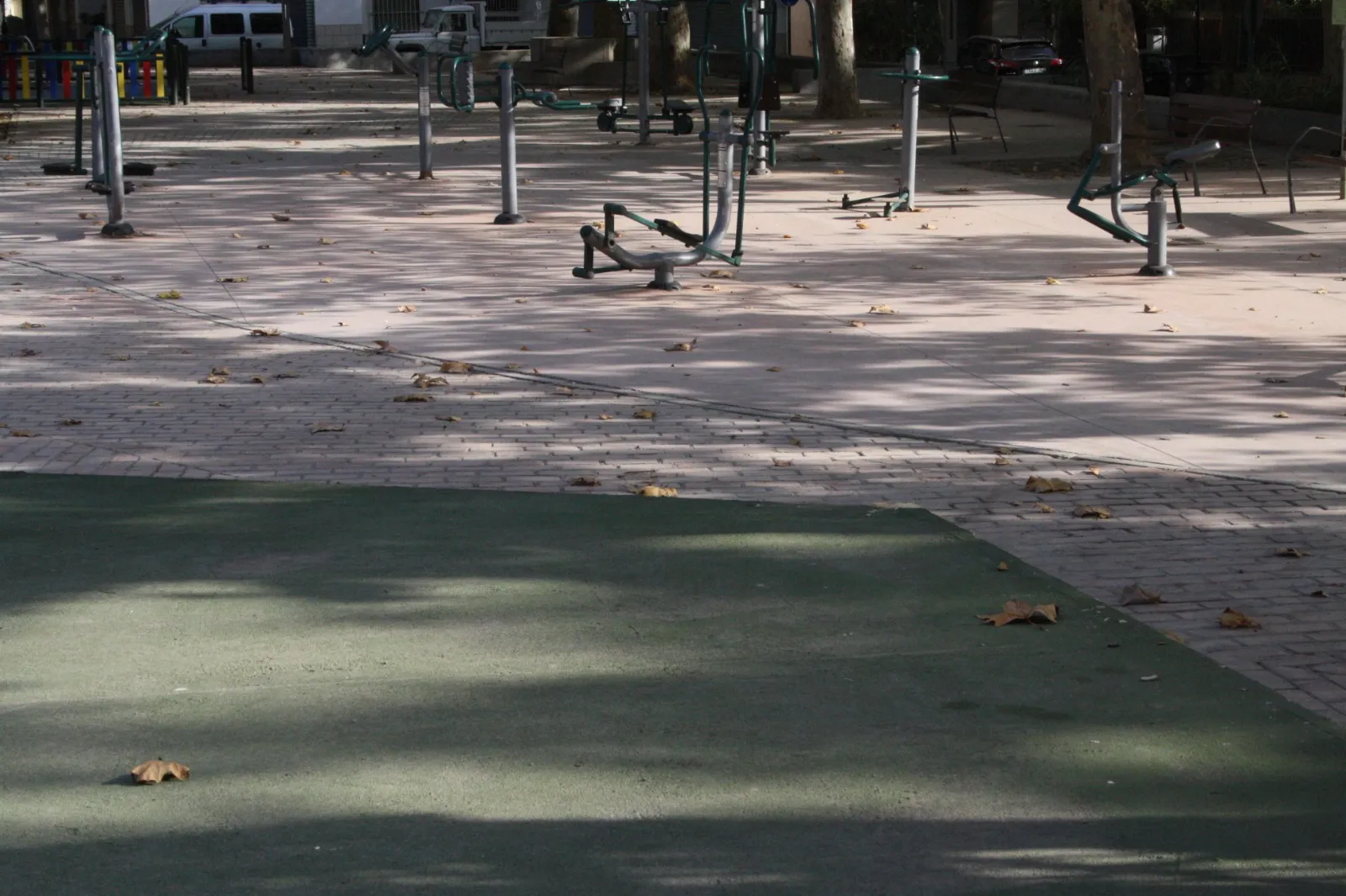 Zona de aparatos de gimnasia al aire libre, vacía, con hojas secas por el suelo