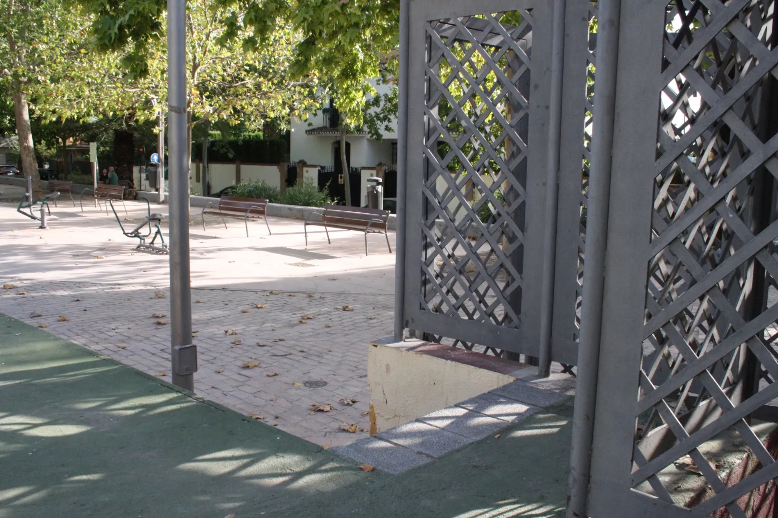 Celosía metálica de una caseta en una plaza, con bancos al fondo